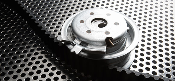 A bearing tensioner and timing belt on a metal perforated surface.