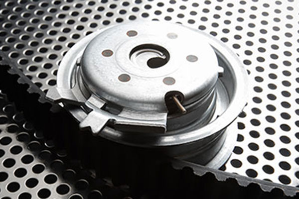 A bearing tensioner and timing belt on a metal perforated surface.