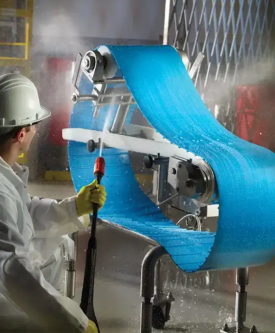 A monolithic conveyor belt being washed with a power washer.