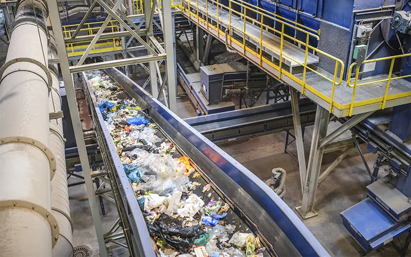 High angle close-up of pieces of recyclable garbage on conveyor belt inside waste management facility.