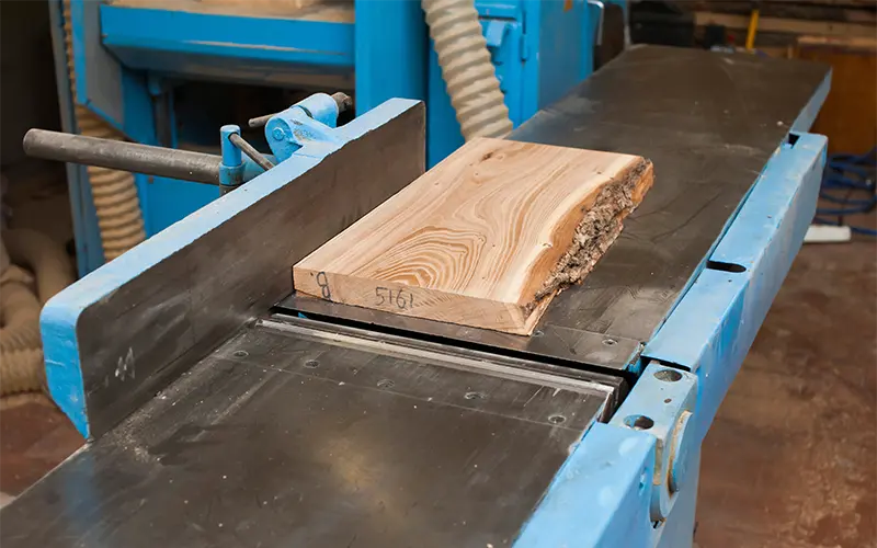 a rough board lies on a large jointer in a carpentry shop. Manufacturing of wooden furniture